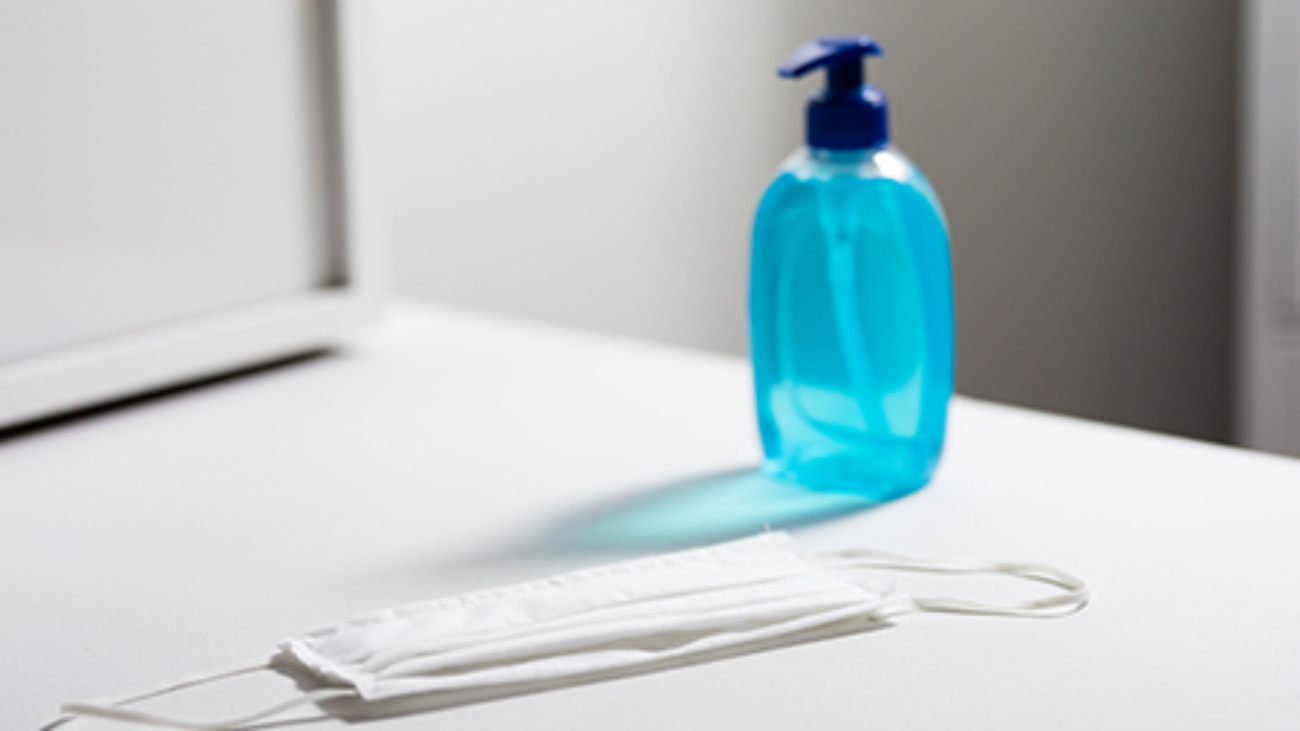 Close up of a sanitizer and white face mask protection against pandemic covid 19 coronavirus and for safety lying on a white table