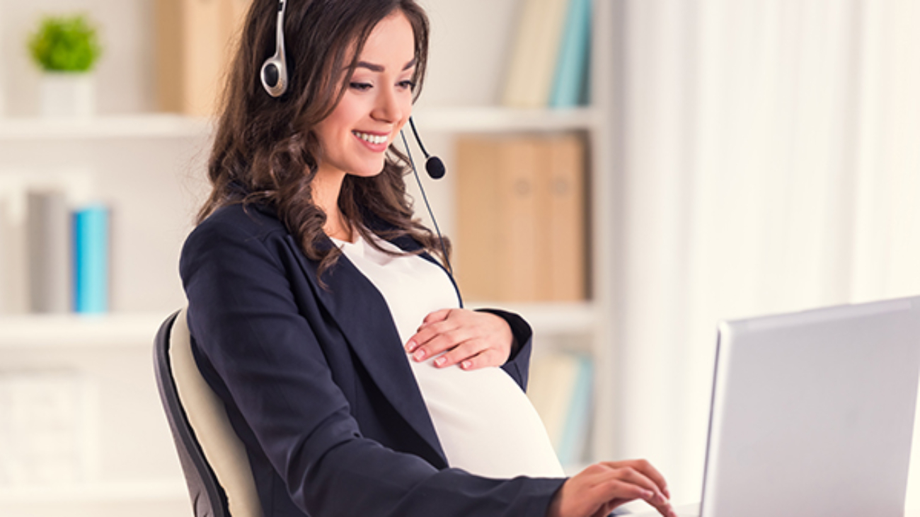 Call center. Young pregnant business woman with headset using a laptop in the office