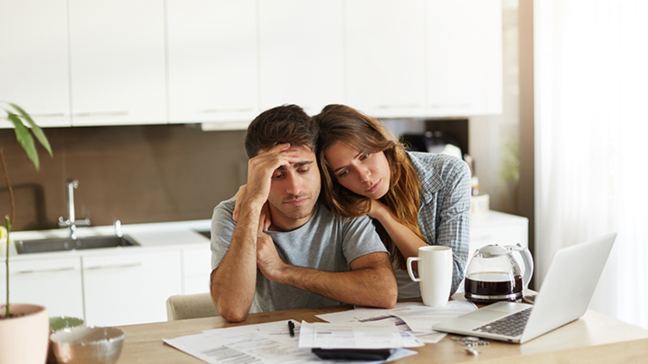 Stressed wife and husband with many debts doing paperwork together, reviewing their expenses, planning domestic budget and calculating bills in kitchen, surrounded with papers, calculator and laptop